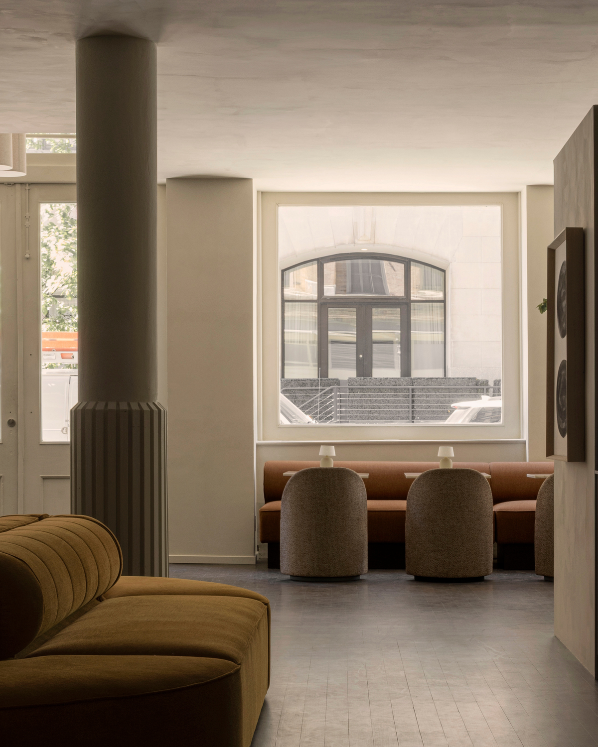 Minimal interior with tan upholstered sofa, rounded beige dining stools and oran