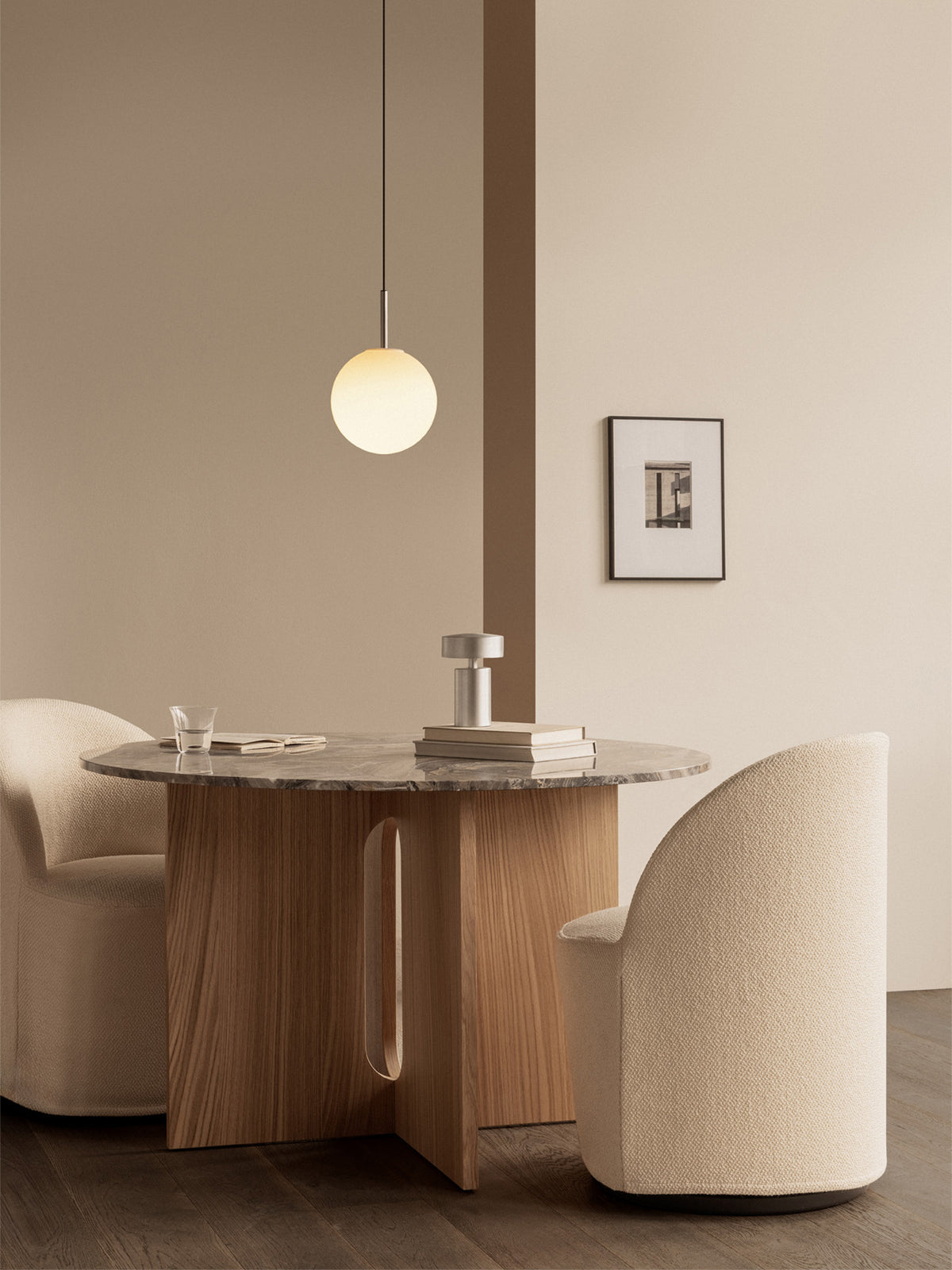 Round opal glass pendant light with brushed metal stem above a marble-top