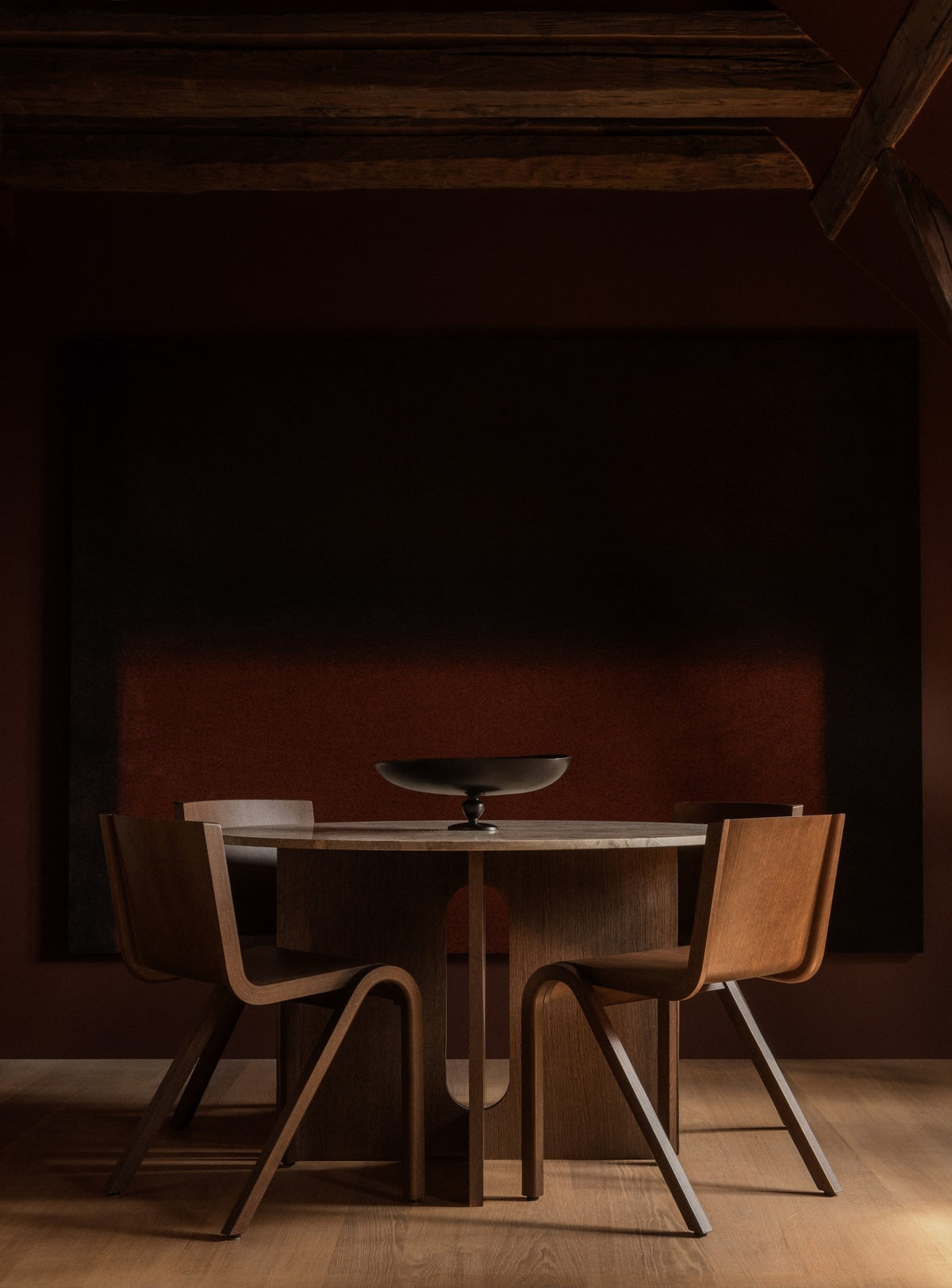 Round wooden dining table with four curved walnut chairs and a low
