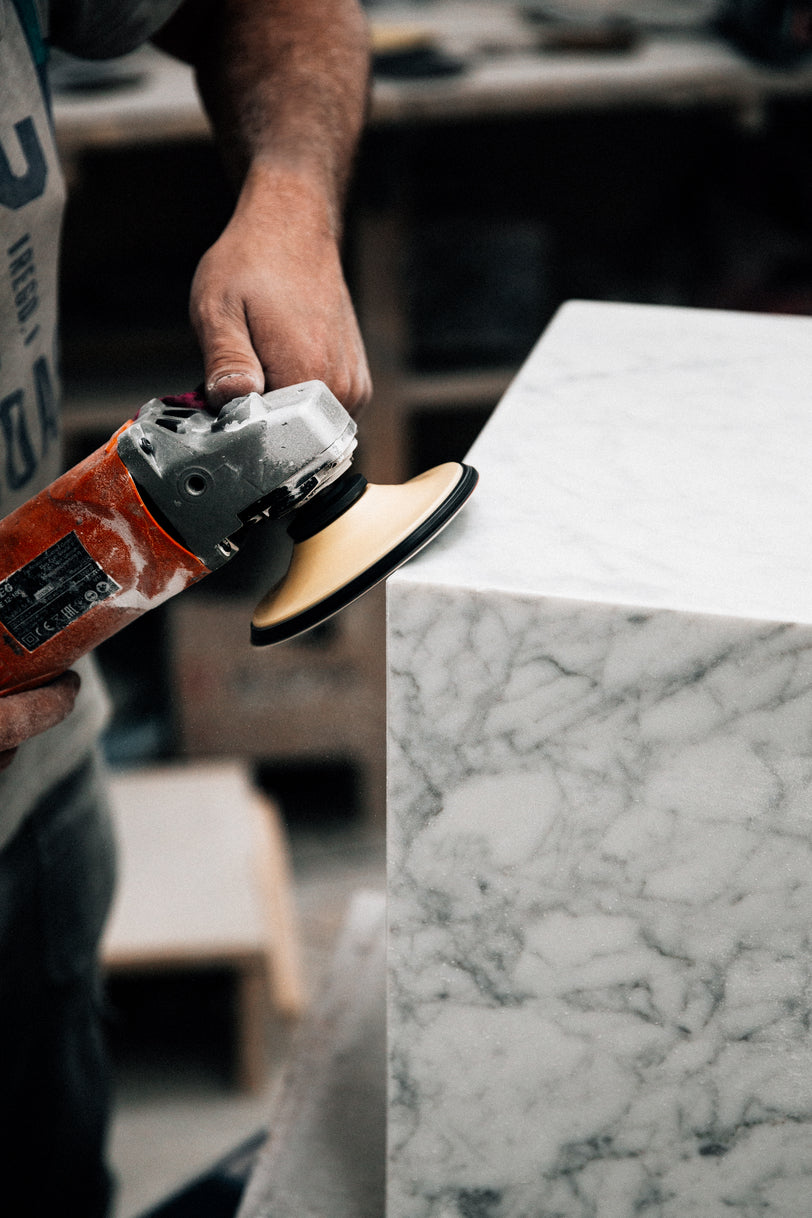 Hand holding an orange power sander polishing the beveled edge of white