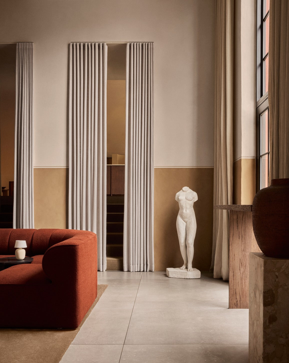 Minimal living room with rust-red curved sofa, beige curtains, tall window, and
