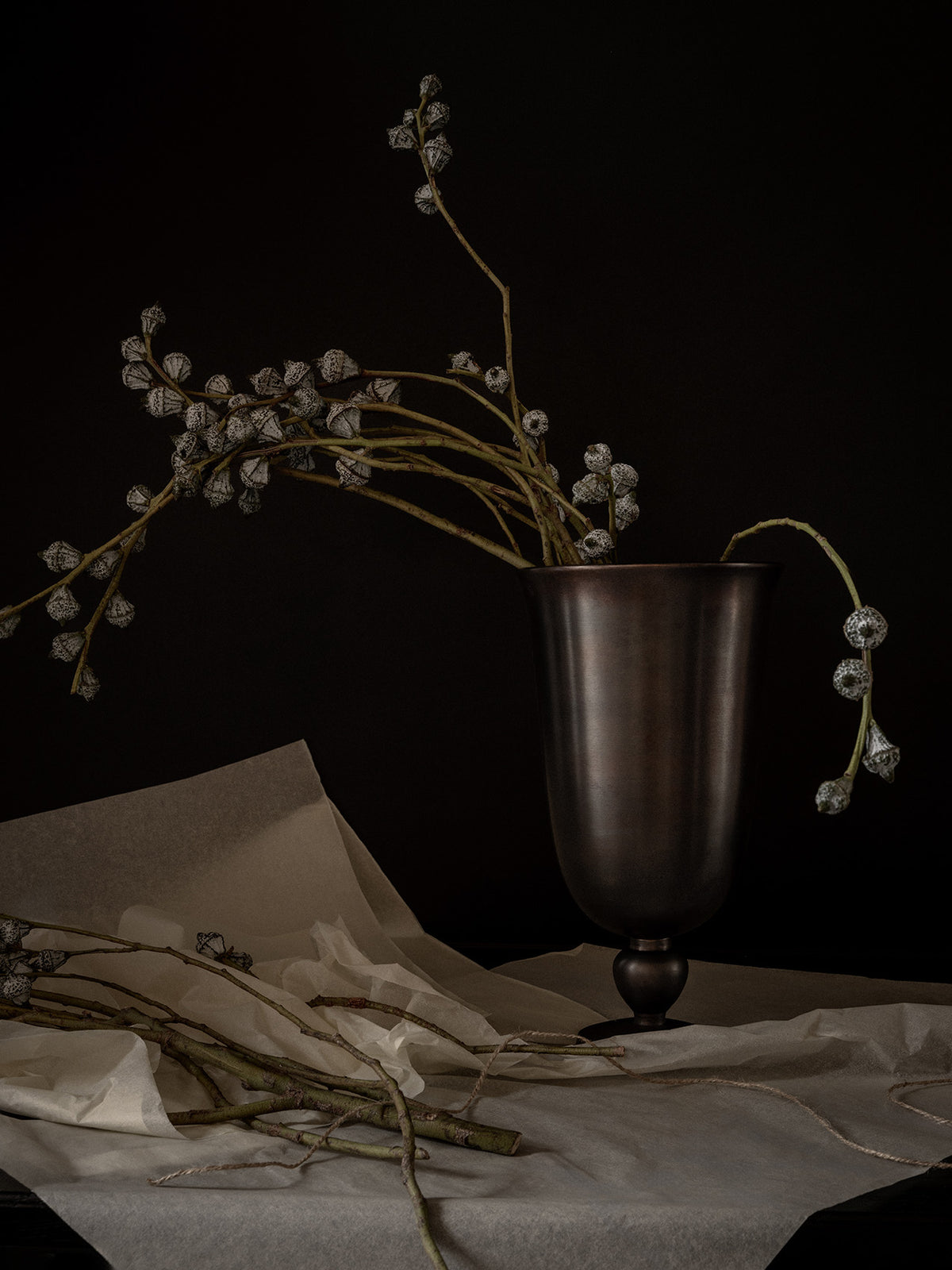 Matte dark metal urn with tall, curved branches of white-speckled seed pods