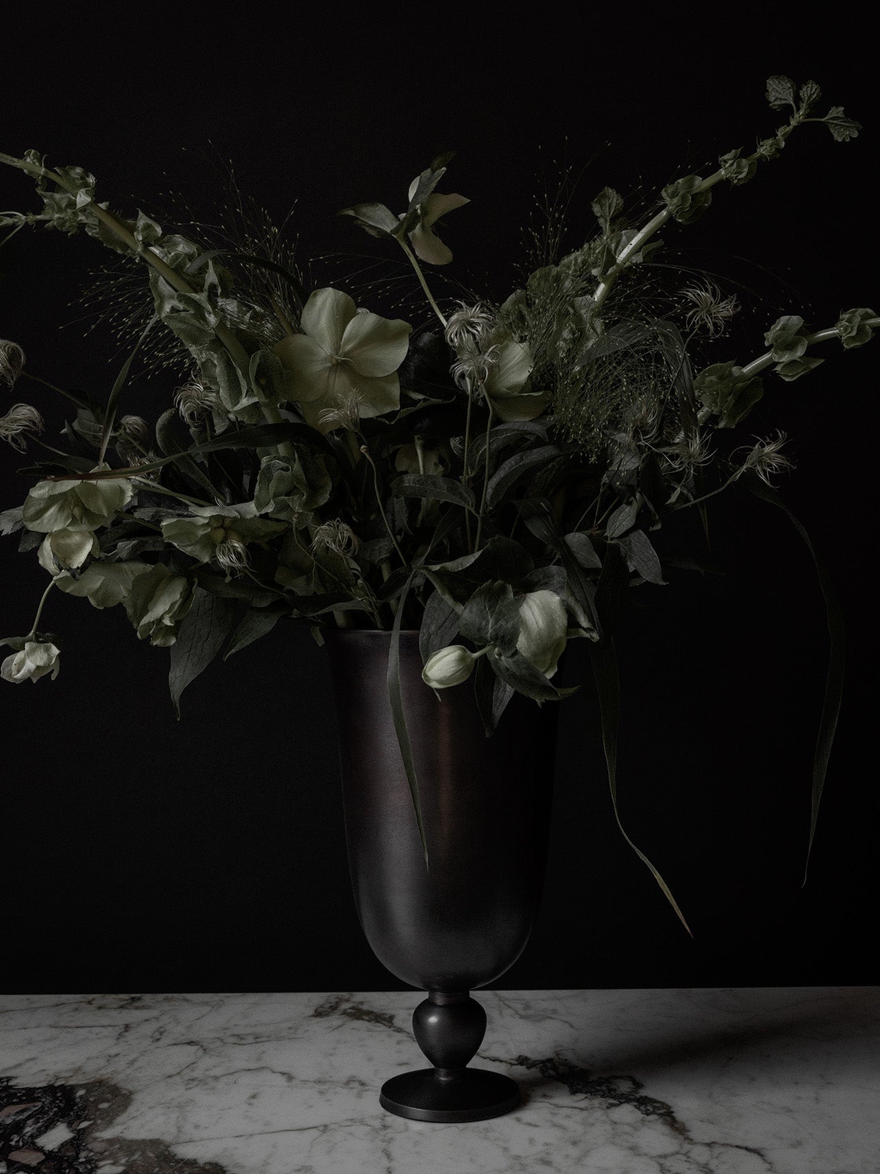 Tall matte black metal vase with loose green foliage and pale green