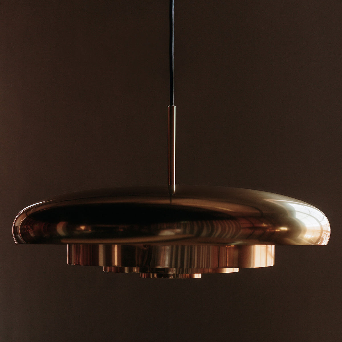 Glossy brass pendant ceiling light hanging against a dark background, showcasing