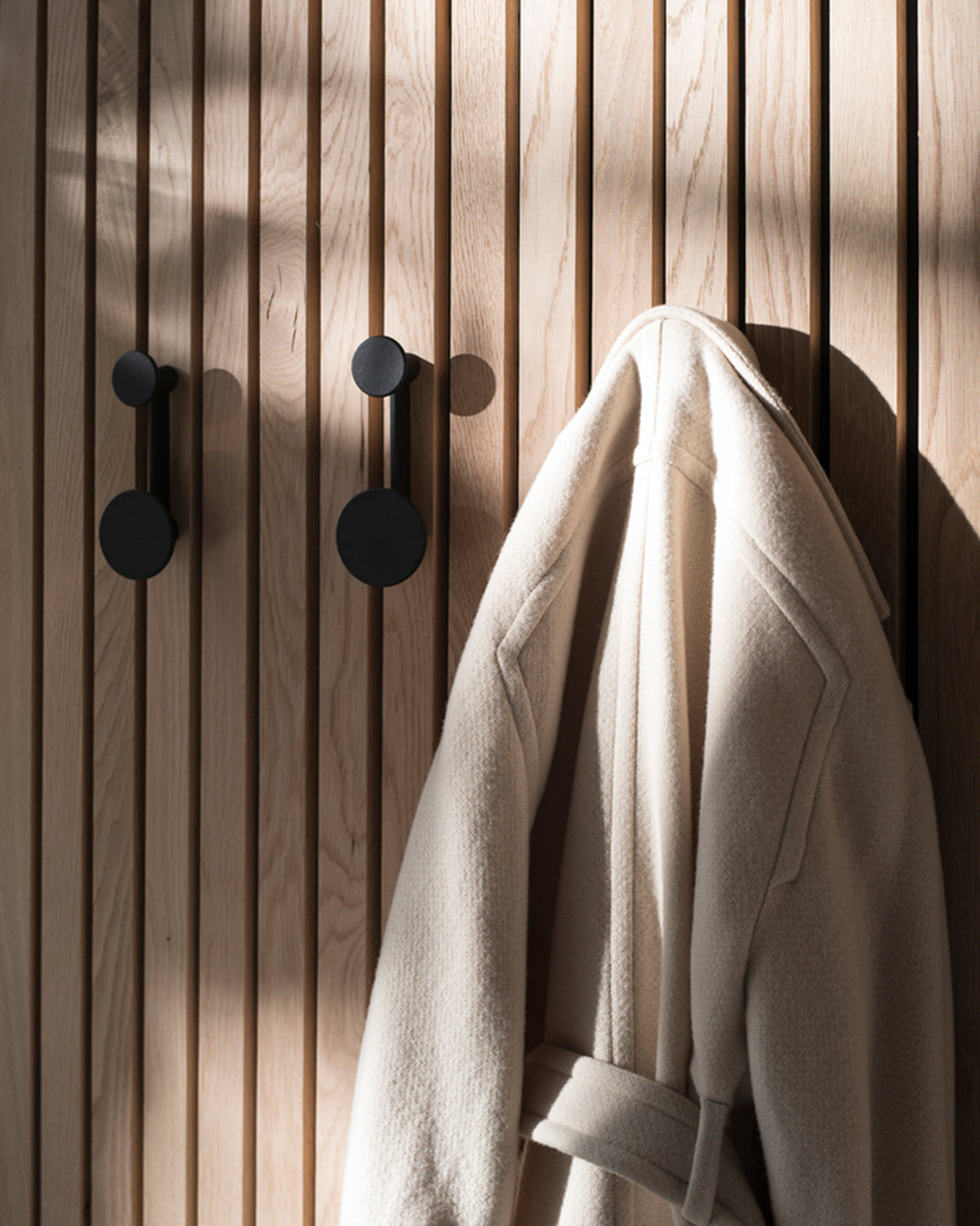 Light oak slatted wall with matte black round coat hooks and a