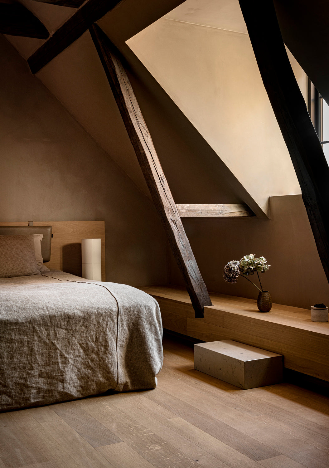 Minimal attic bedroom with beige linen bed, wooden beams and low oak