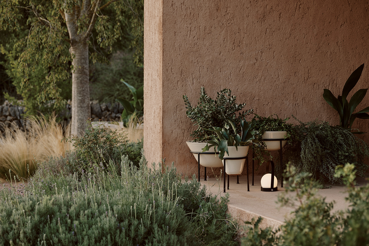 Outdoor scene with beige ceramic planters on black metal stands, green foliage,