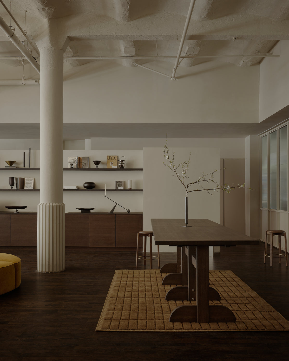 Minimalist dining table scene with dark wooden table, brown textured rug, slim
