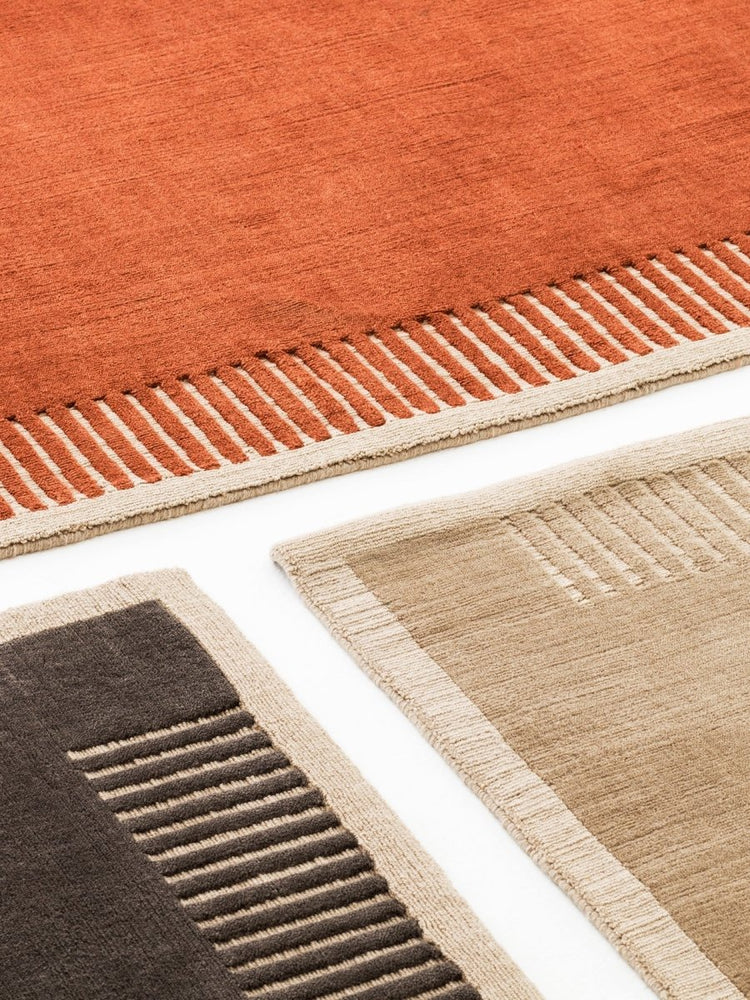 A detailed close-up of three Duomo Rugs in terracotta, dark brown, and beige, showcasing textured pile and linear patterns.
