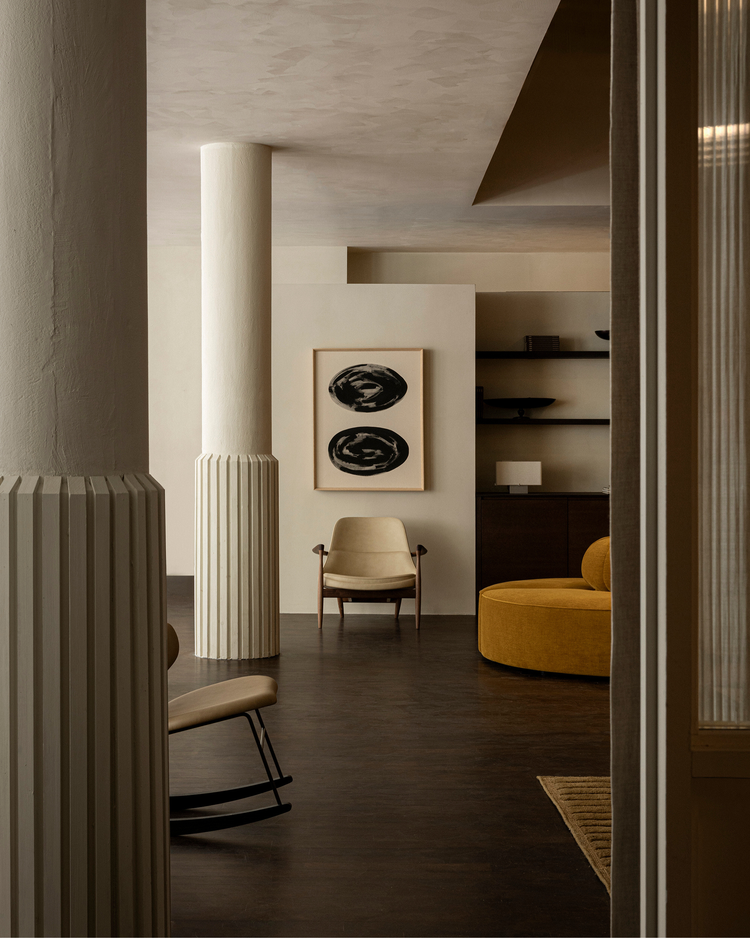 Minimalist interior with fluted off-white columns, beige leather armchair, framed black abstract prints and mustard round