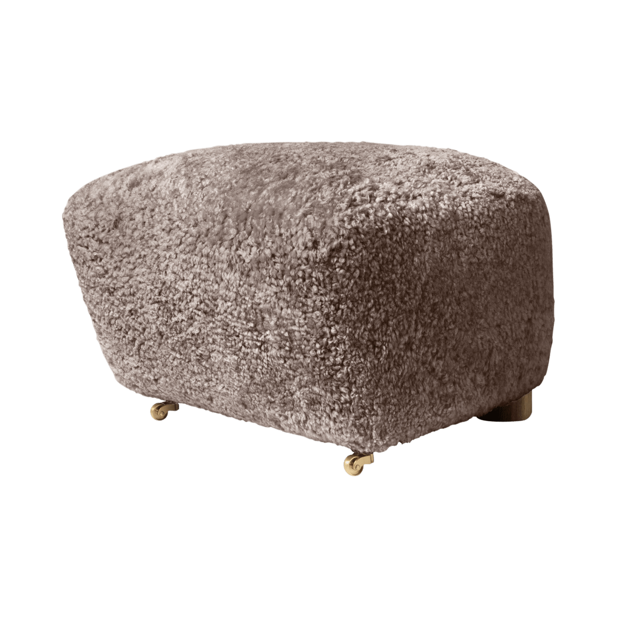 The Tired Man Ottoman upholstered in dark sheepskin, featured on small brass castor wheels against a white background.