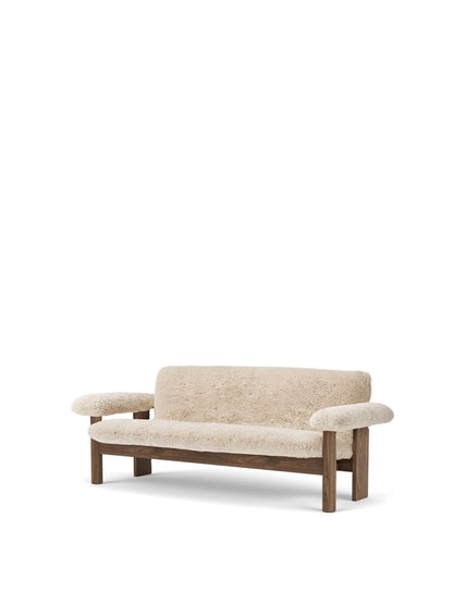 An angled view of the Brasilia Sofa in Sheepskin, showing its plush, off-white upholstery and dark-stained solid wood frame.