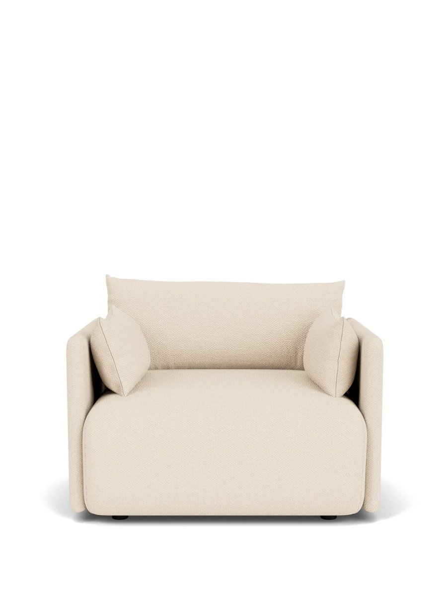 Beige upholstered lounge chair with textured fabric, rounded block seat, low back and two matching bolster cushions.