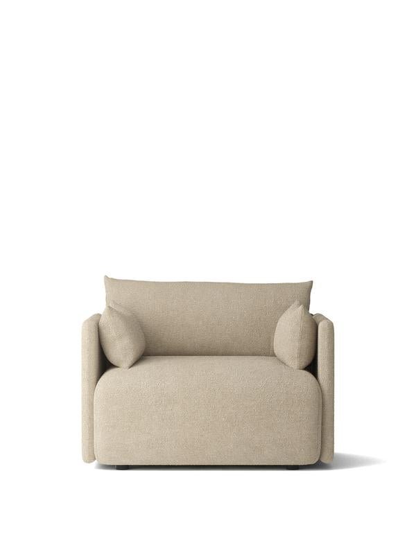 Beige boucle upholstered lounge chair with rounded edges, low back and two cylindrical arm cushions, front view on white