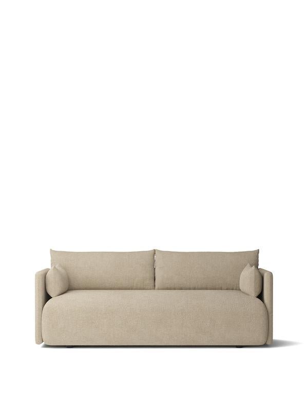 Beige upholstered three-seater sofa with rounded edges, low profile back cushions and cylindrical bolster pillows, fabric