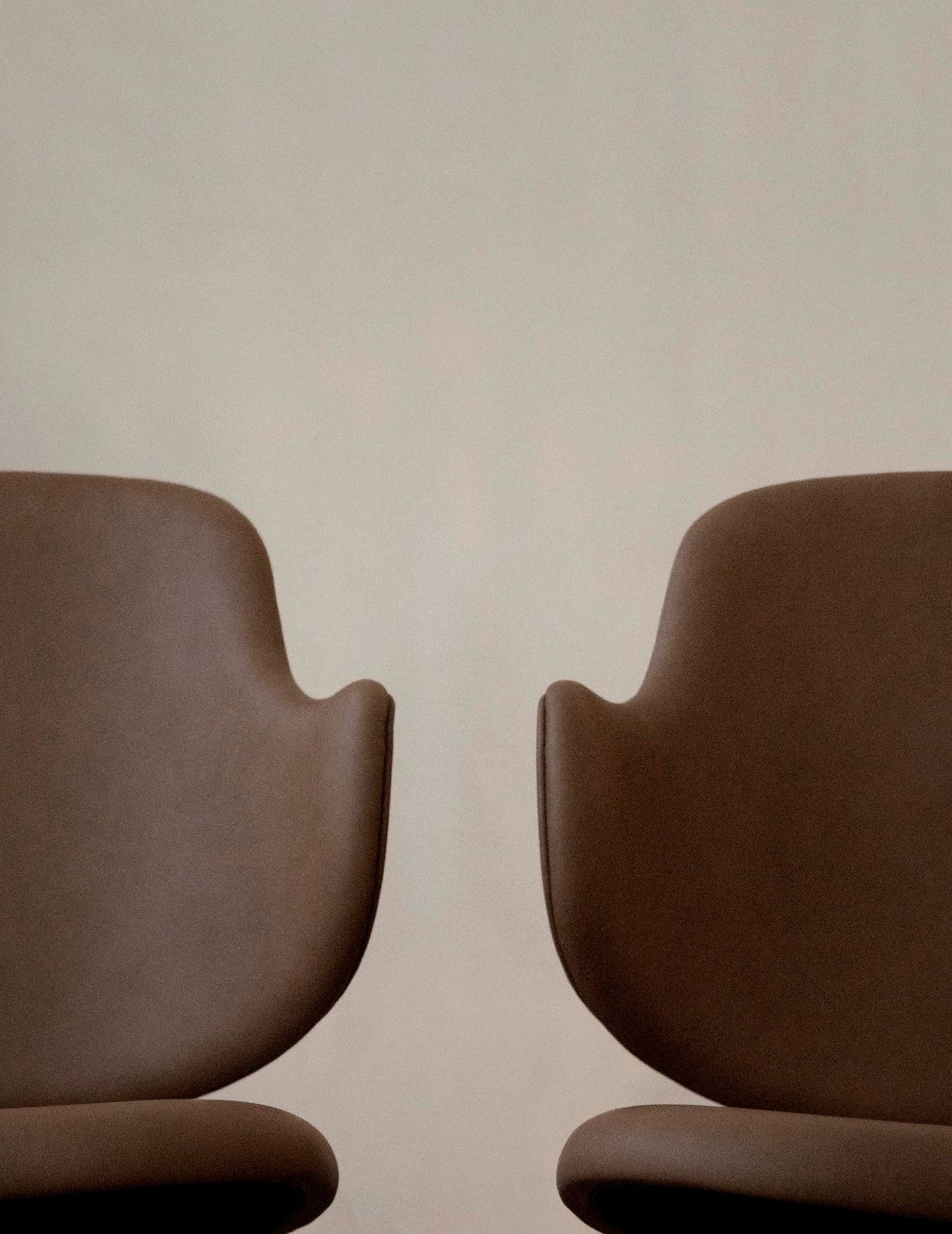 Close-up of two brown leather curved chair backs and seats against a pale neutral background