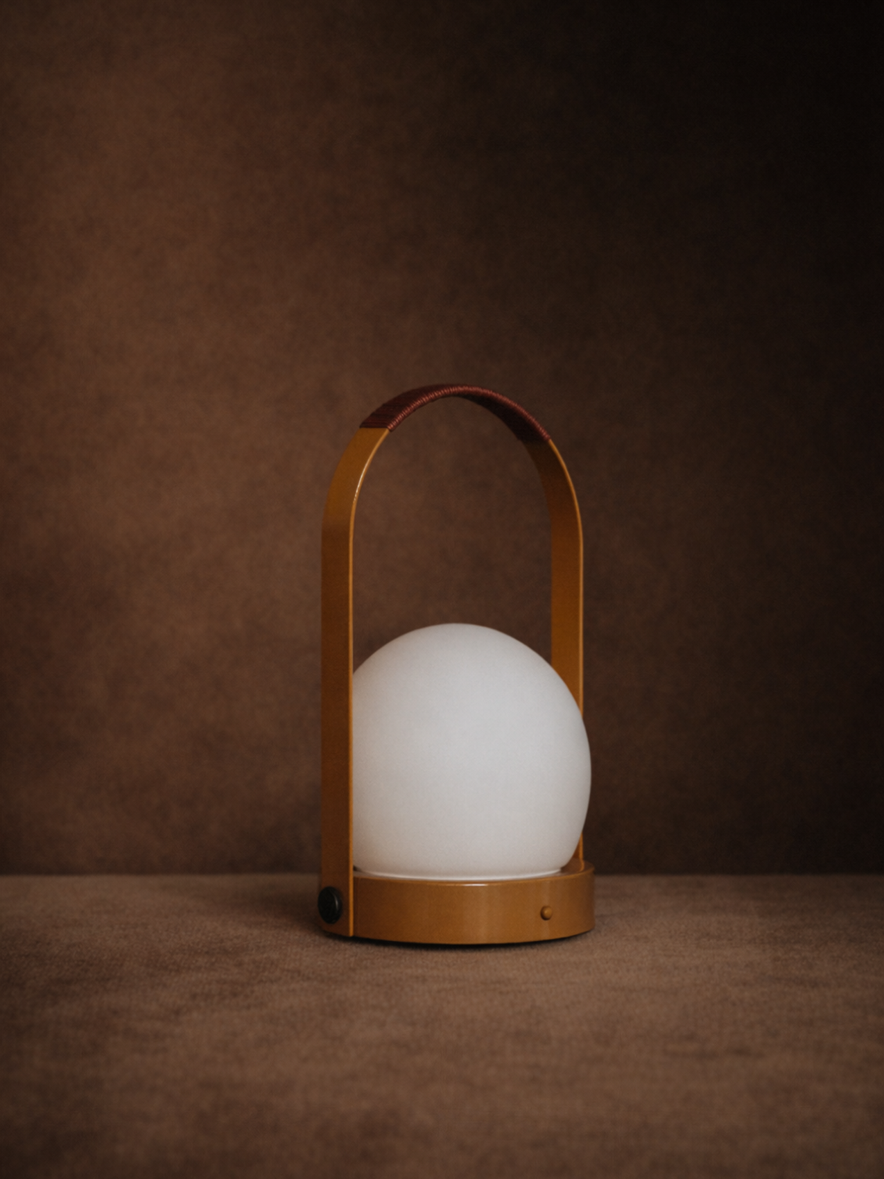 Carrie Portable Lamp in Golden Brown, featuring a leather-wrapped handle and opal glass globe against a dark backdrop.