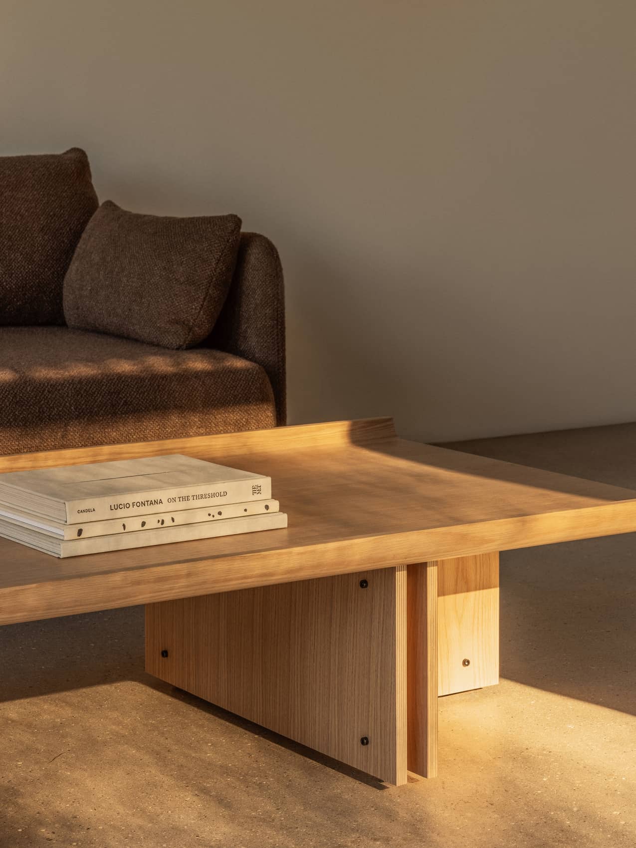 Natural oak Conrad Lounge Table with curved edges and exposed screws, styled next to a textured brown Offset Sofa.