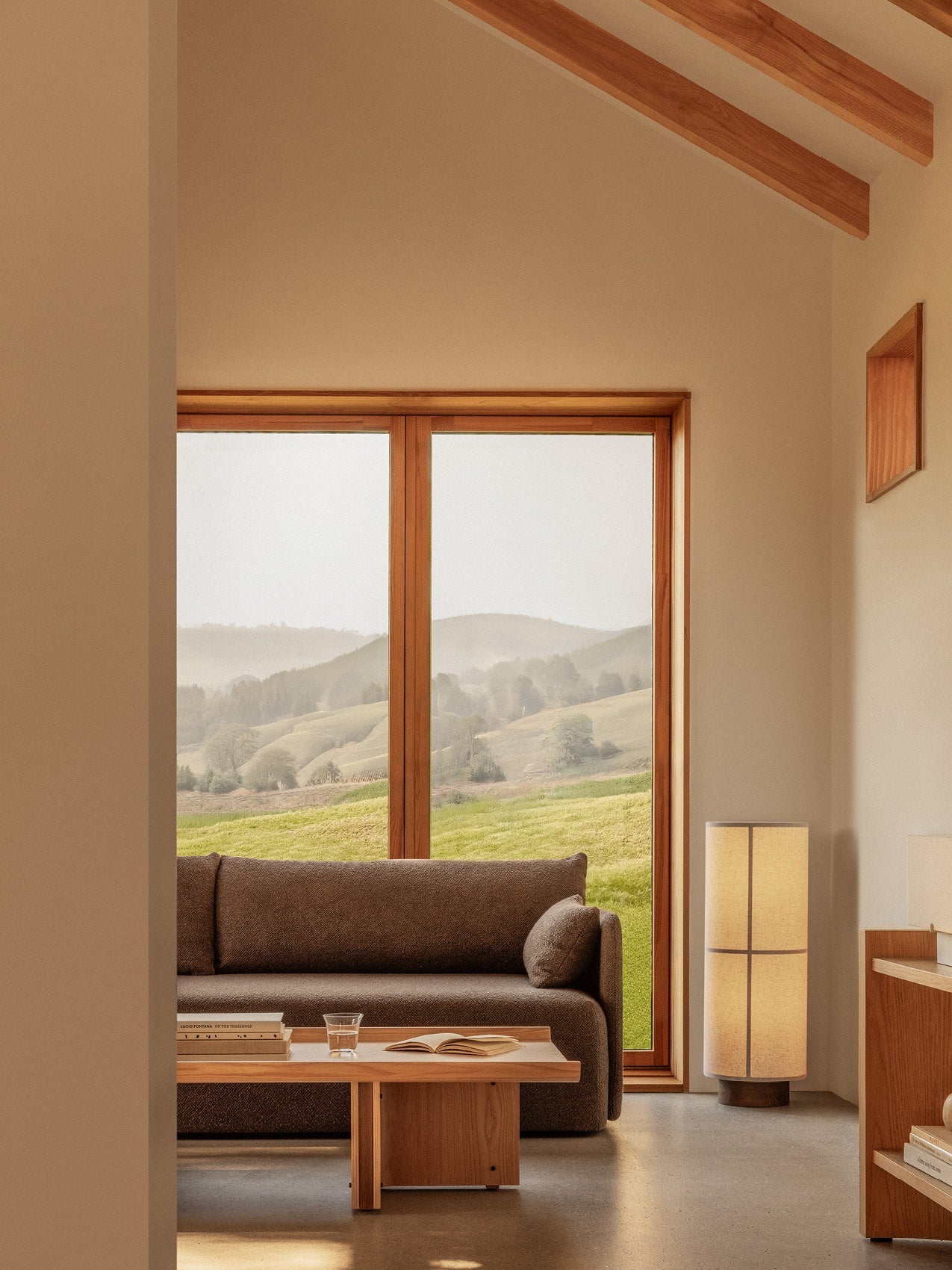 Natural oak Conrad Lounge Table and Offset Sofa in a bright room with a Hashira Floor Lamp and scenic window views.