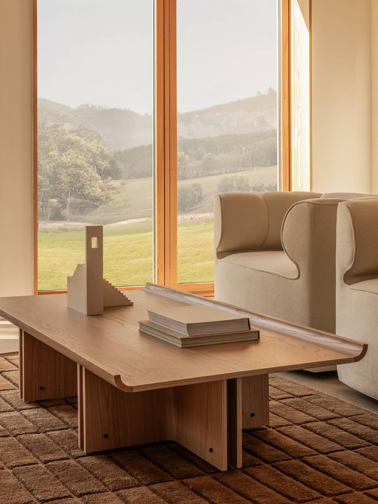 Natural oak Conrad Lounge Table on a Tile Rug, paired with Eave Seamline Lounge Chairs overlooking a scenic landscape.