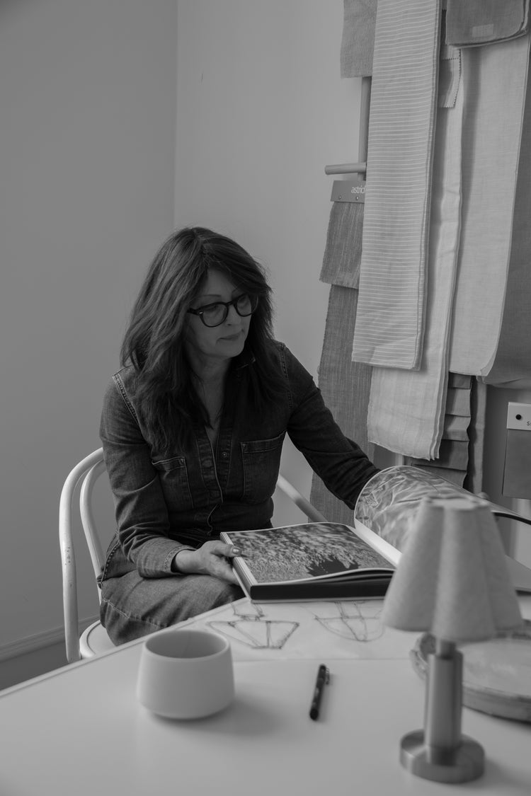 Studio scene with neutral linen fabric samples hanging on a wooden rail and a person browsing a large design book