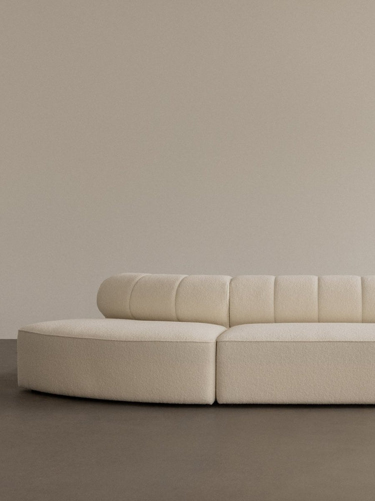 A close-up of the Eave Seamline Modular Sofa in cream bouclé, with its curved form and detailed backrest stitching.