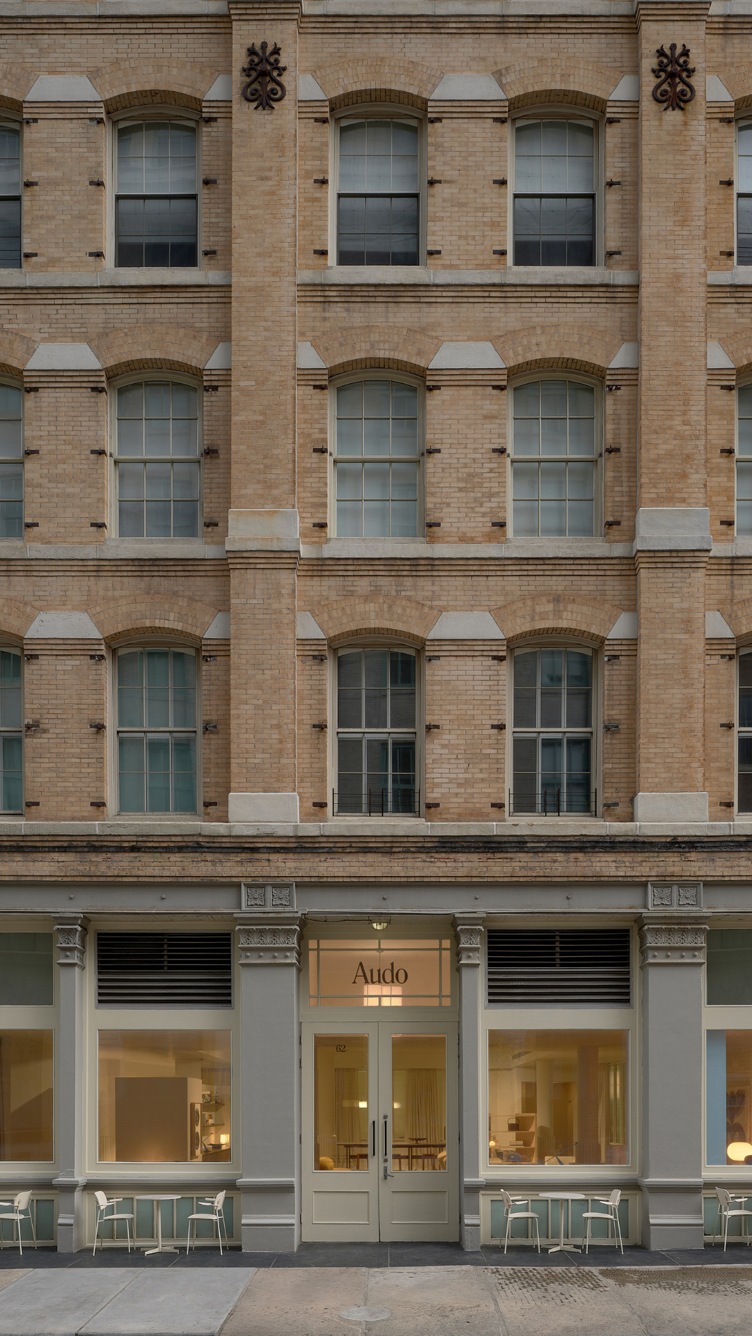 Exterior storefront of Audo Copenhagen in beige brick building with tall arched windows and pale gray entrance, outdoor