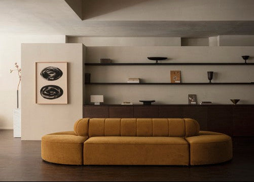 Mustard-yellow curved modular sofa in velvet with low back and rounded ends in minimalist living room composition.
