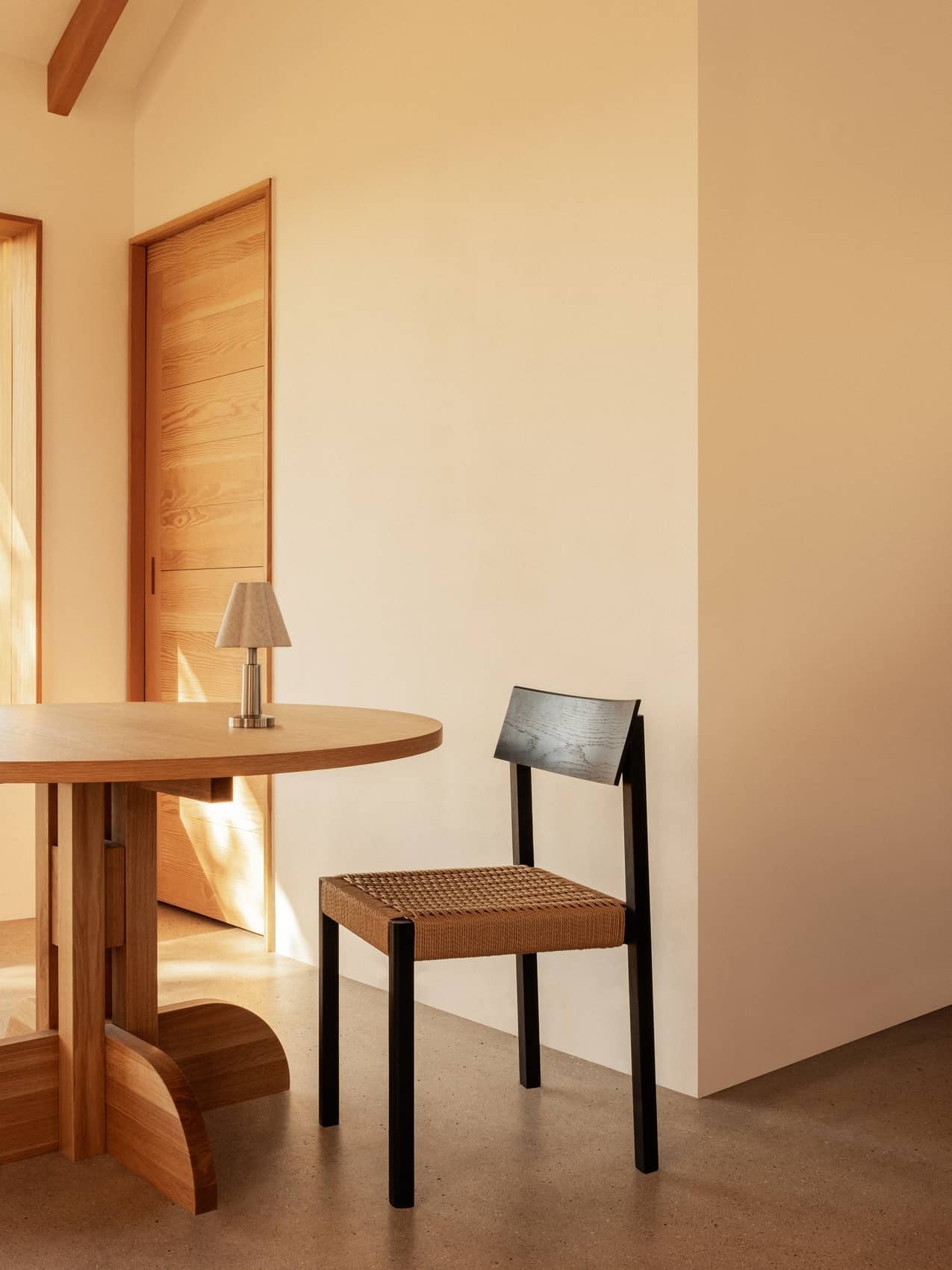 Black oak Mauro Dining Chair with a paper cord seat beside a Puffin Dining Table and Admiral Portable Table Lamp.