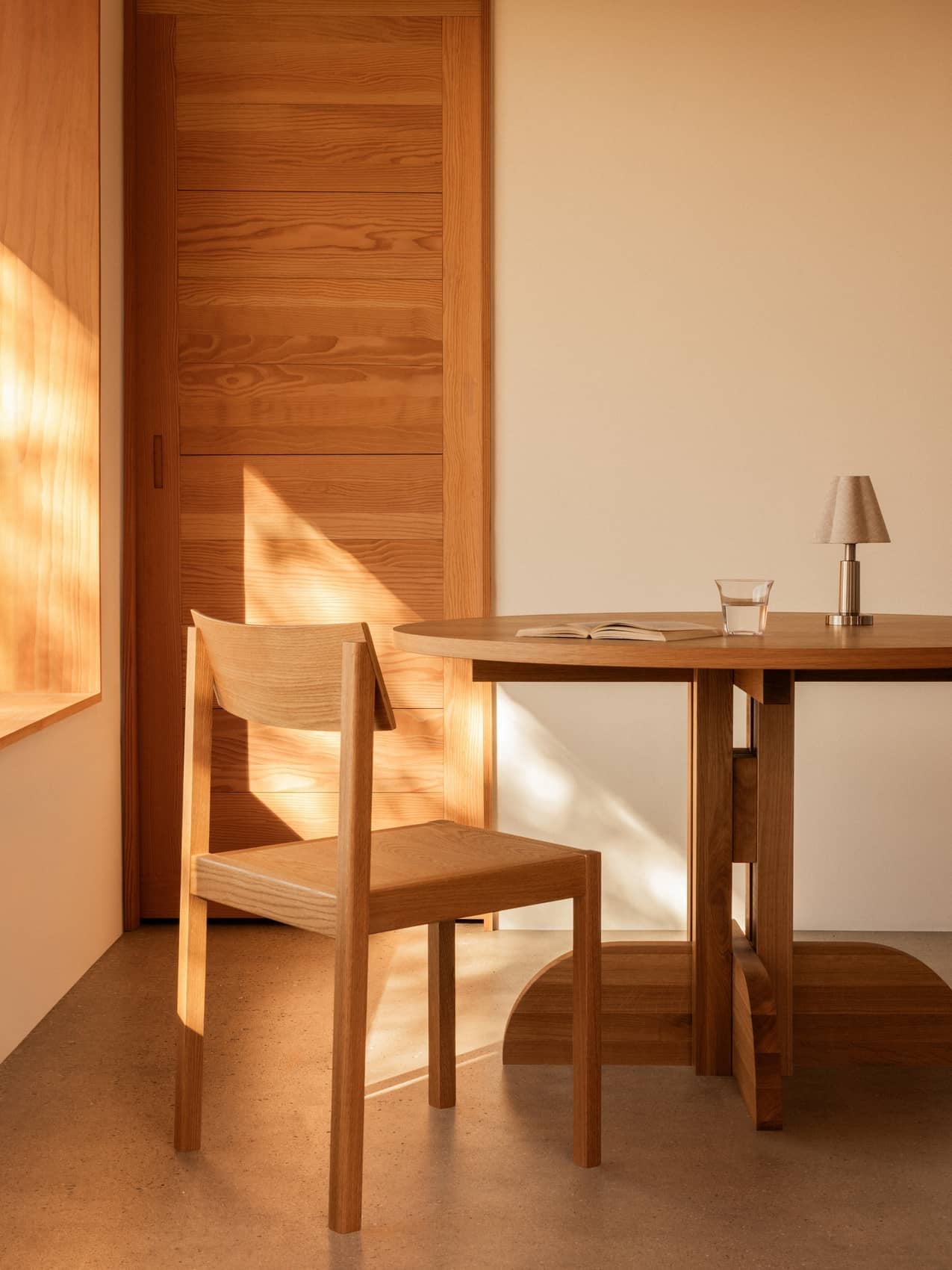 Admiral Portable Lamp on a wooden Puffin Dining Table beside a Mauro Dining Chair in a warm, sunlit room.