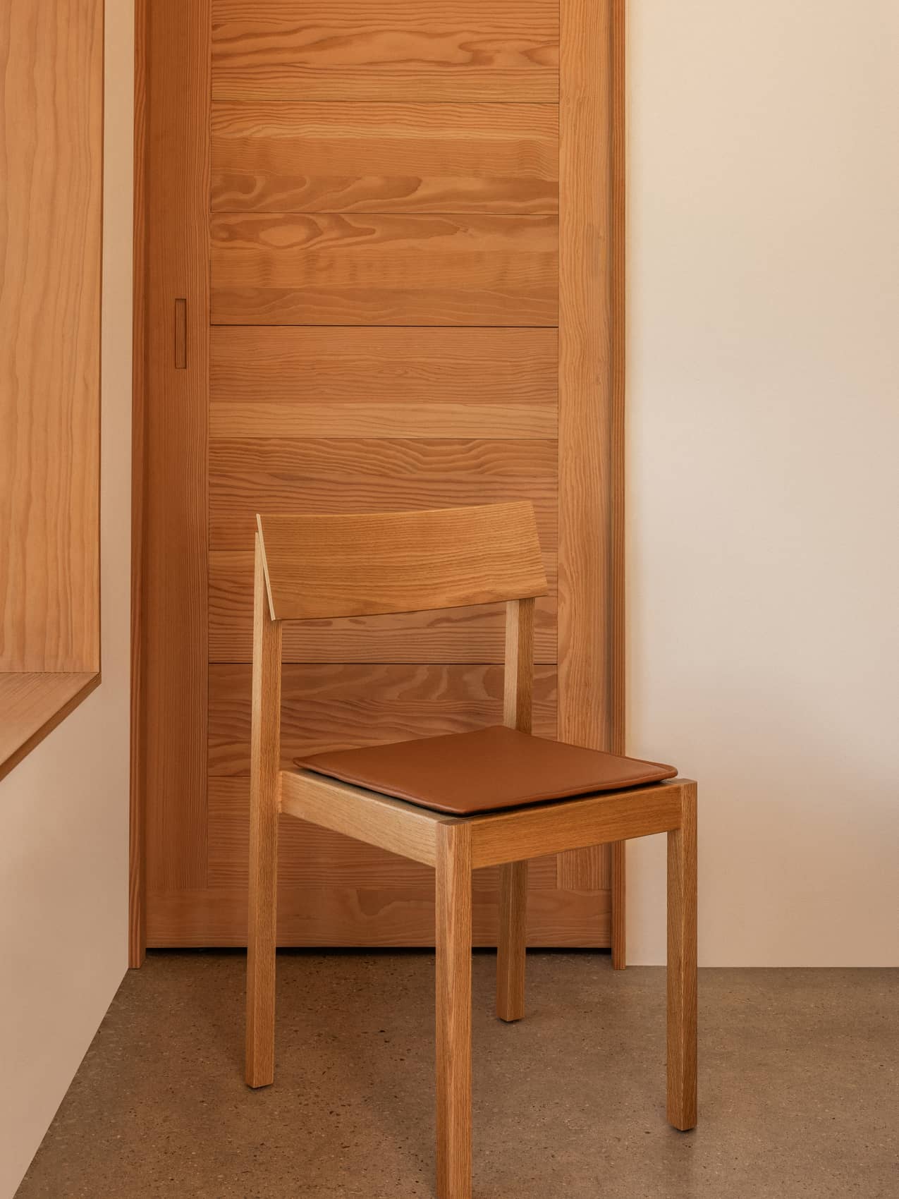 Mauro Dining Chair in light oak with a cognac leather Mauro Dining Chair Seat Cushion in a minimalist setting.