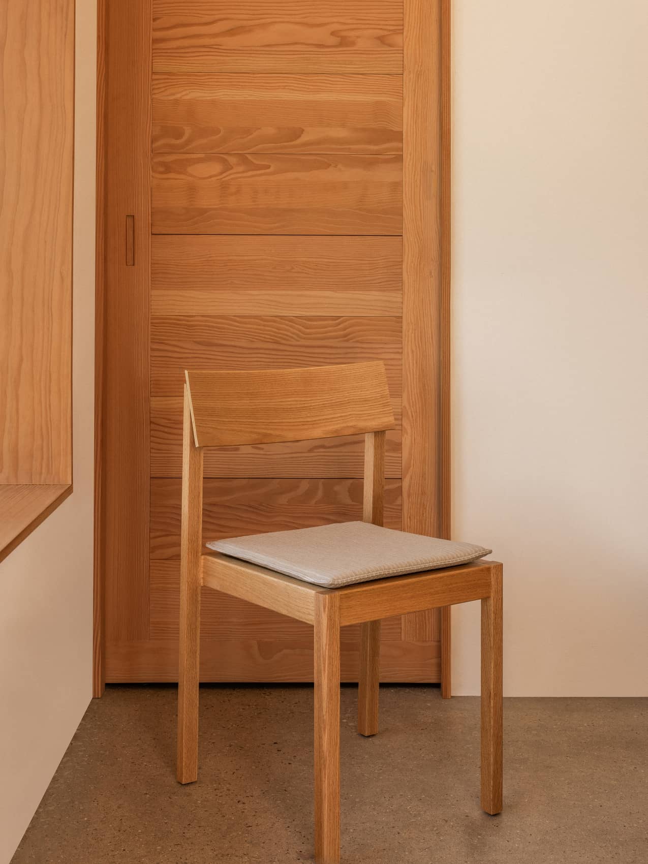 Mauro Dining Chair Seat Cushion in light textile on a wooden Mauro Dining Chair against a warm timber door.