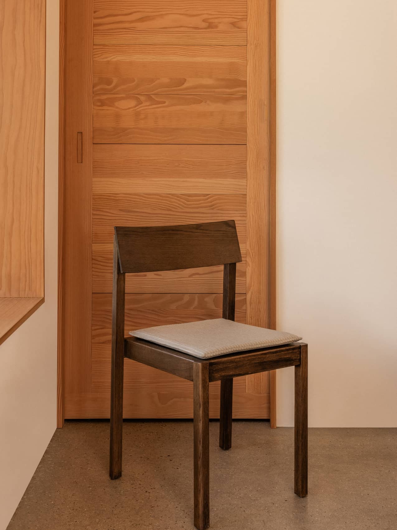 Dark wood Mauro Dining Chair with a light grey Mauro Dining Chair Seat Cushion in a minimalist room.