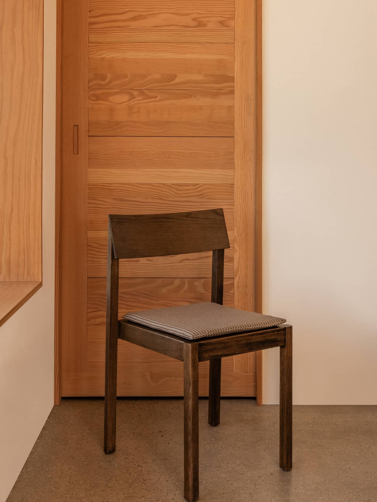 Dark stained oak Mauro Dining Chair featuring a striped seat cushion, set against a light wood panelled sliding door.