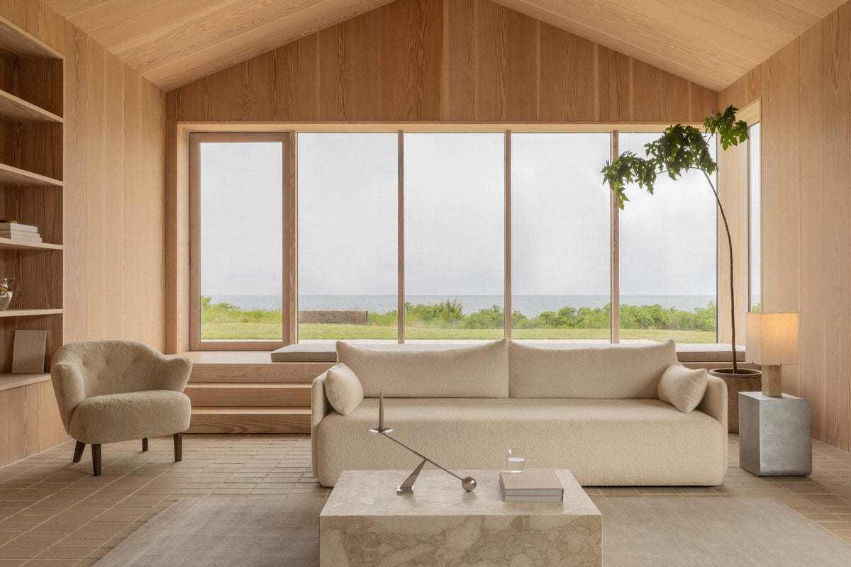 Minimal Scandinavian living room with beige boucle sofa and armchair, light oak walls, large paneled window facing sea