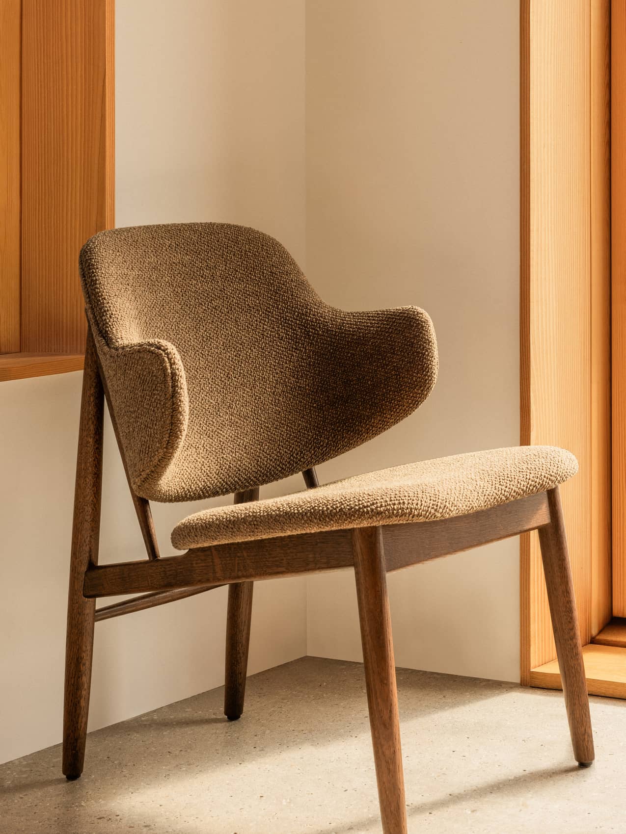 The Penguin Wooden Lounge Chair, fully upholstered in Logan Nutmeg fabric, styled in a minimalist interior corner.