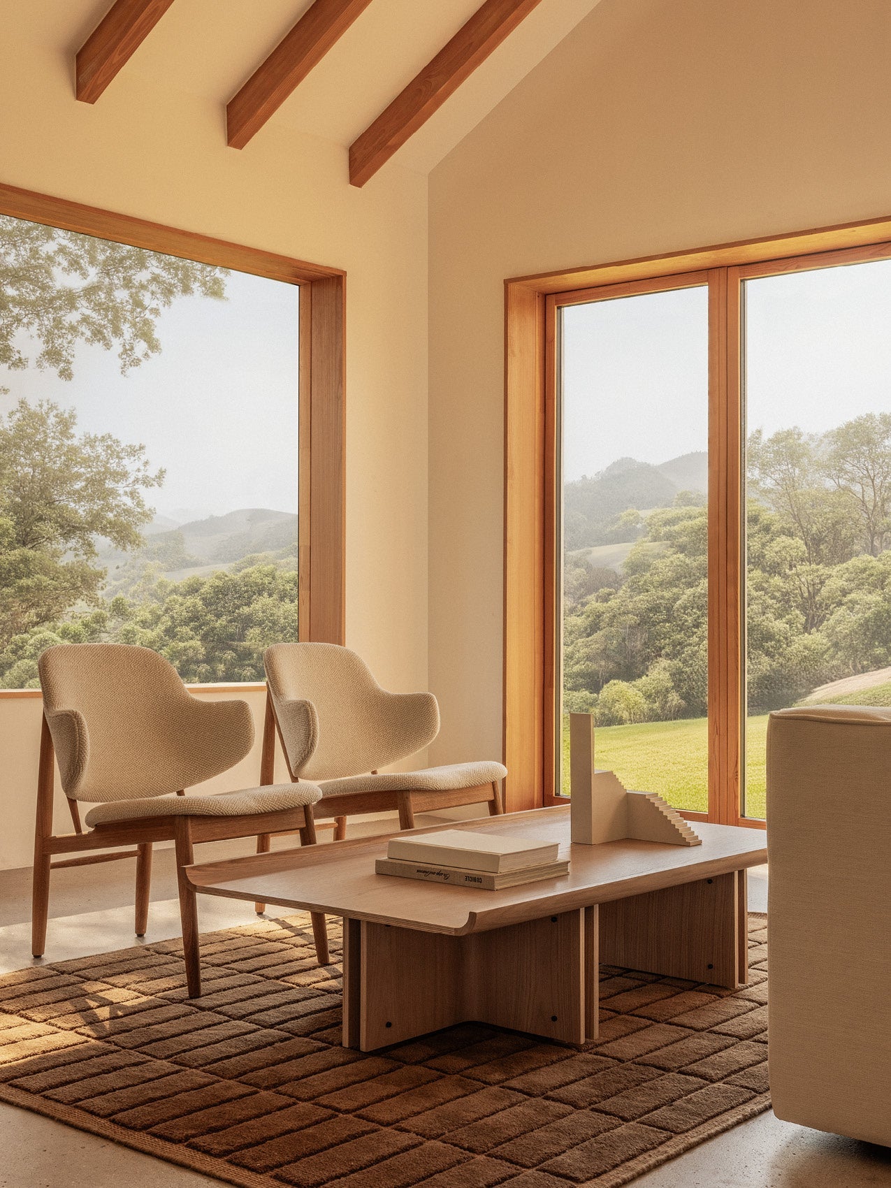 Two Penguin Wooden Lounge Chairs in Logan Fossil and a Conrad Lounge Table on a brown Tile Rug with a scenic backdrop.