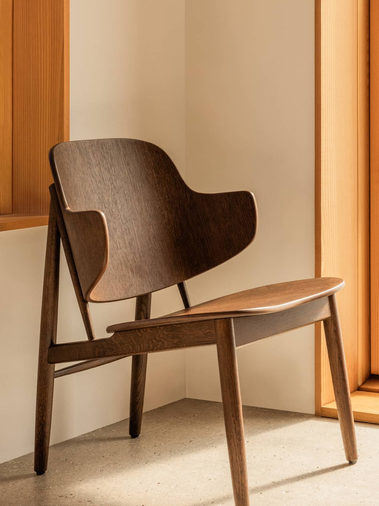 The Penguin Wooden Lounge Chair in red-stained oak, showcasing its curved, unupholstered form in a minimalist interior.