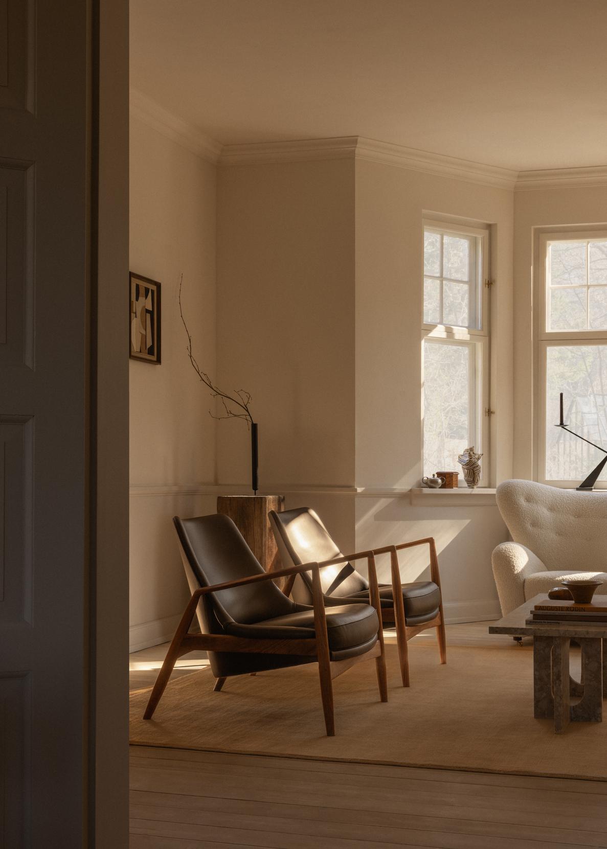 Pair of mid-century wooden frame lounge chairs with dark leather seats in sunlit neutral living room.