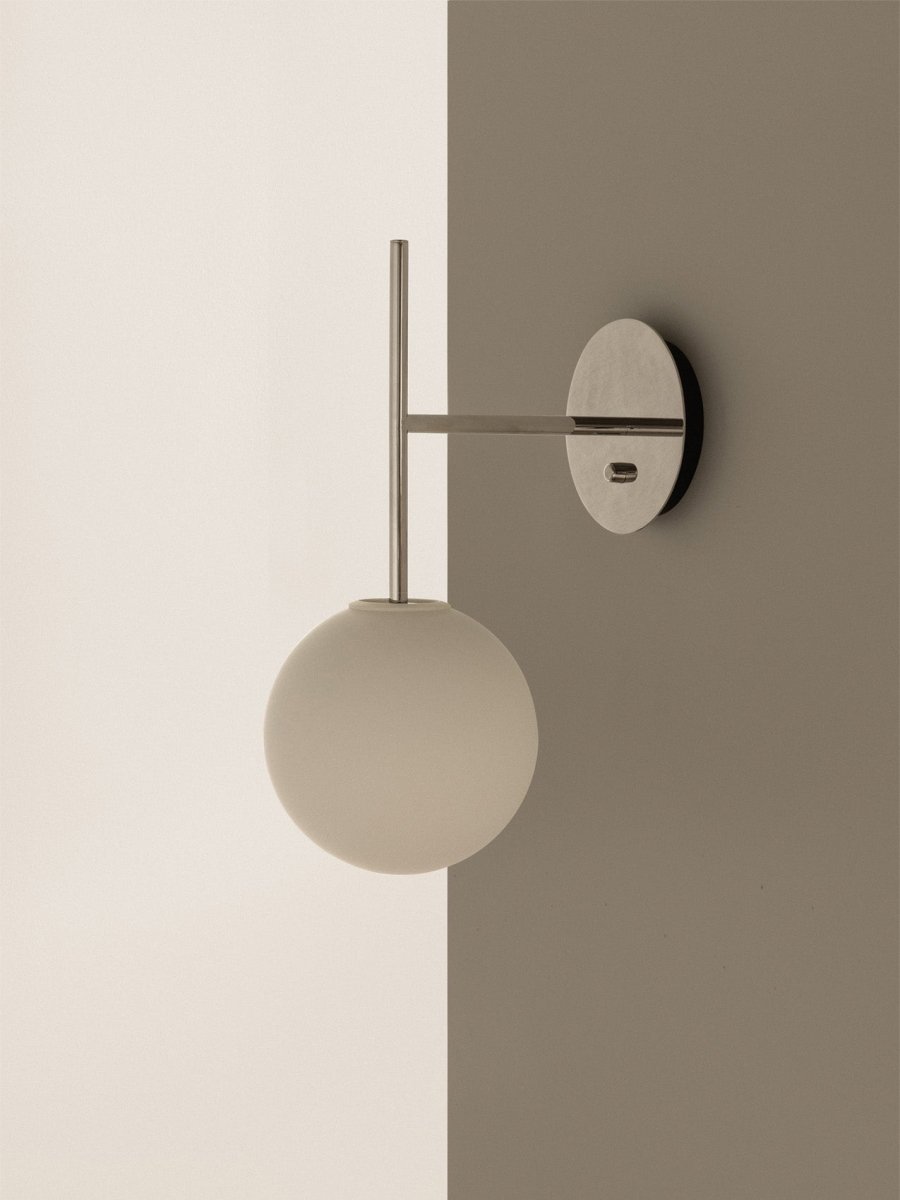 Close-up of the TR Bulb Suspended Wall Lamp in polished steel with an opal glass bulb, on a two-toned white and gray wall.