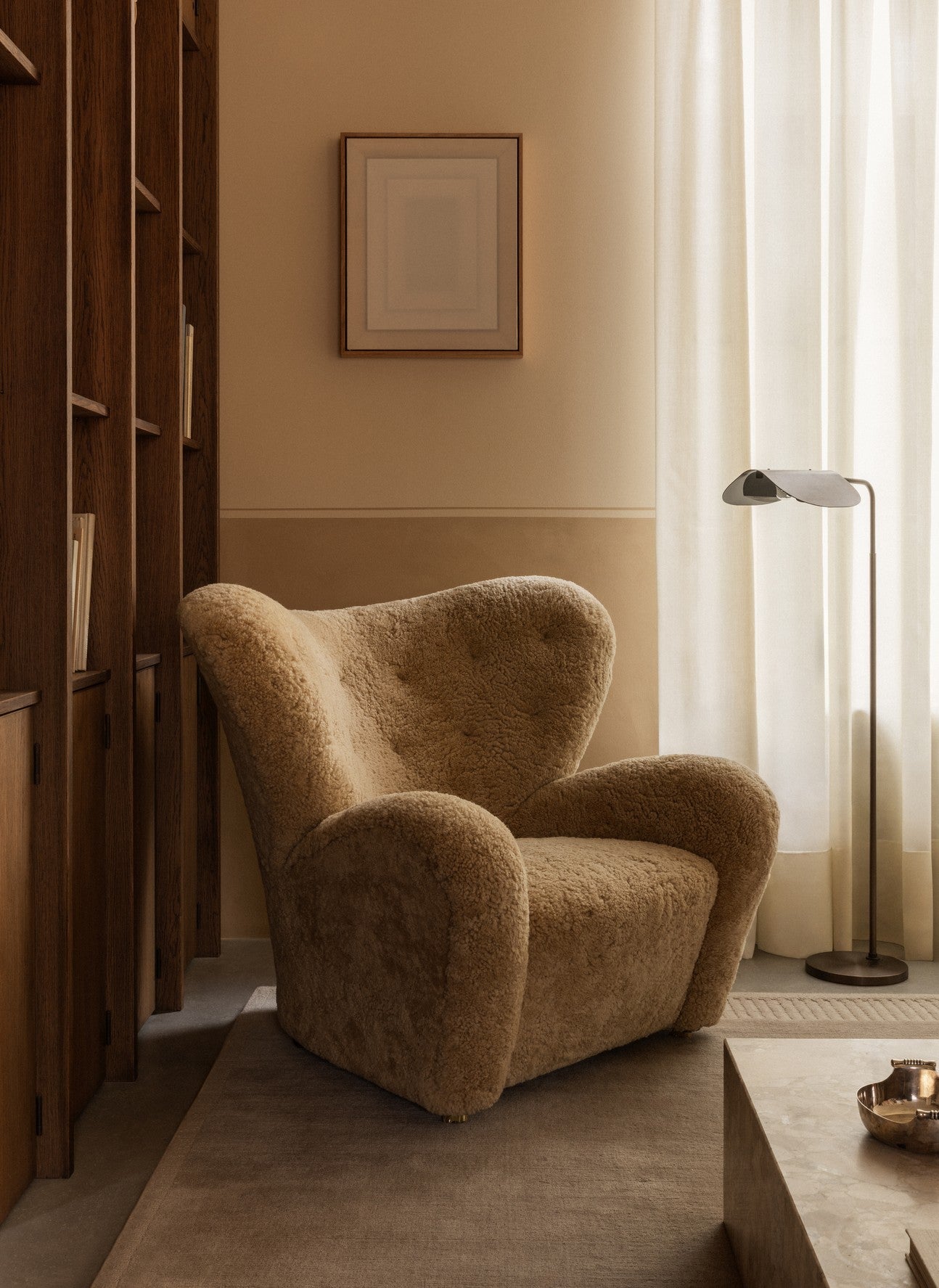 Plush teddy-shearling armchair in warm beige beside wooden shelving, sheer curtains and a slim metal floor lamp