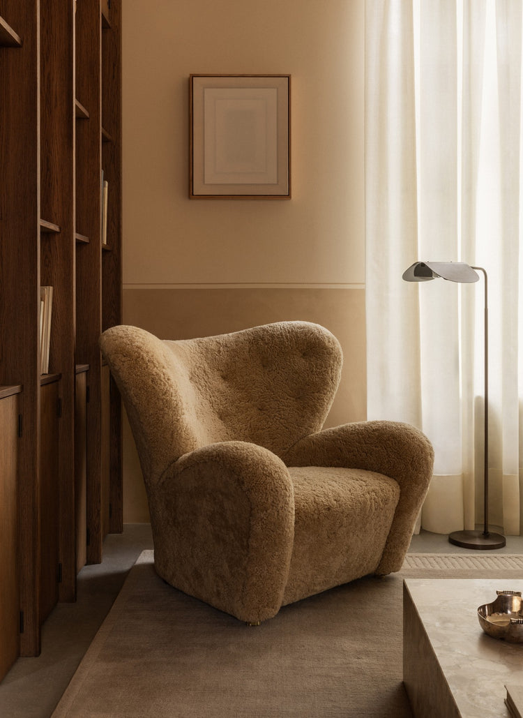 Plush teddy-shearling armchair in warm beige beside wooden shelving, sheer curtains and a slim metal floor lamp