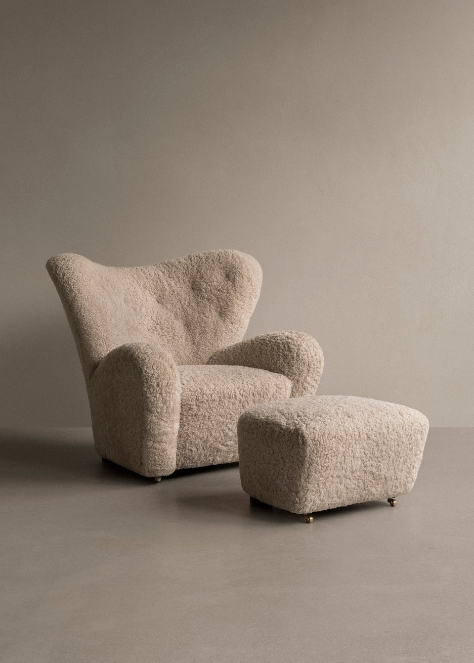 Beige boucle upholstered lounge chair with rounded wingback and matching square ottoman on small brass casters.