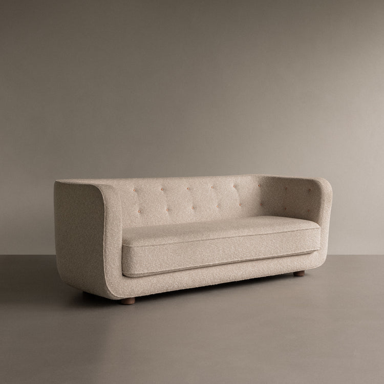 Beige boucle three-seater sofa with rounded arms, button-tufted back and wooden low legs on neutral background