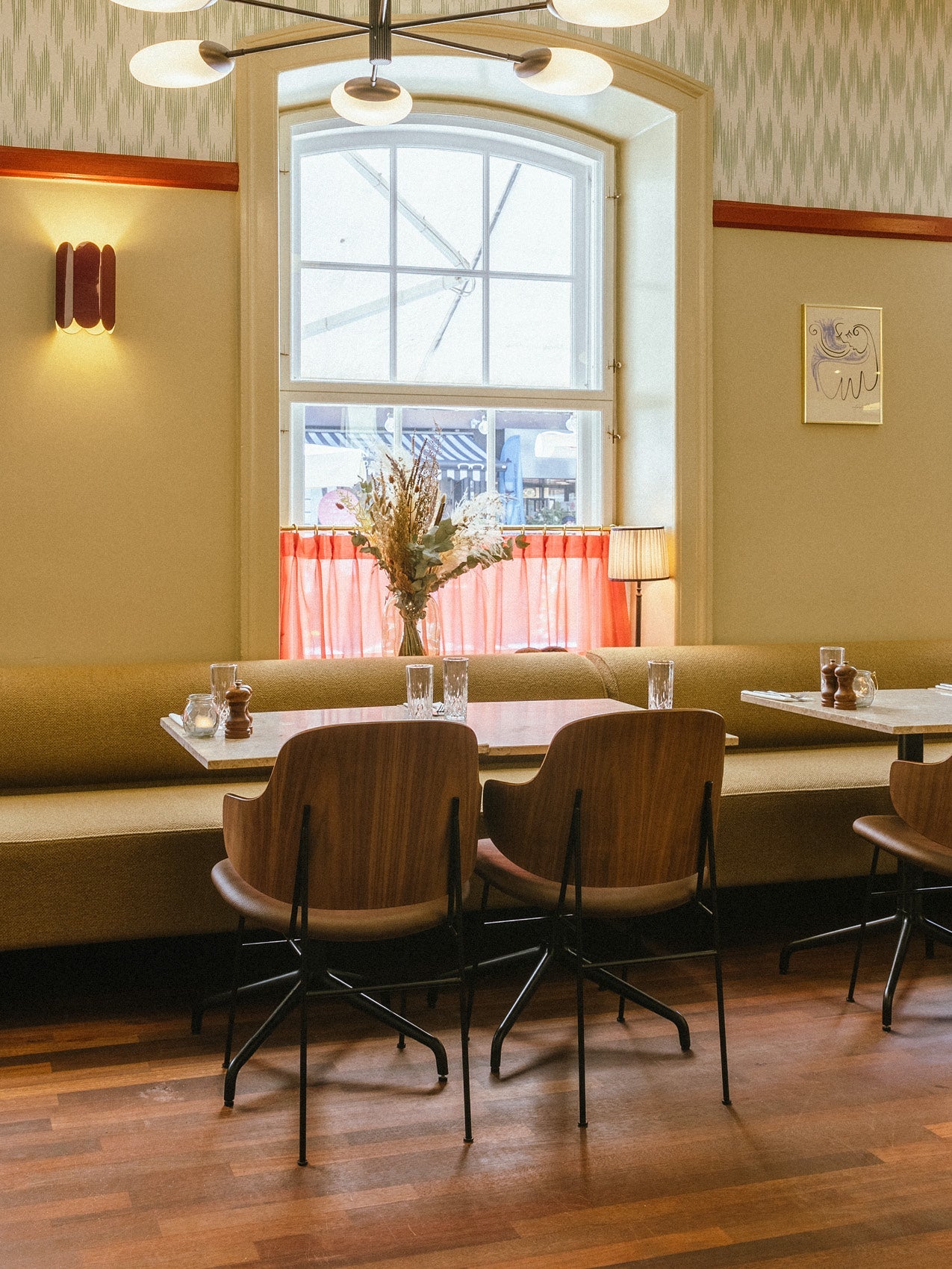 Cozy café seating with wooden swivel chairs, beige banquette, marble tables, glassware and a large arched window with red