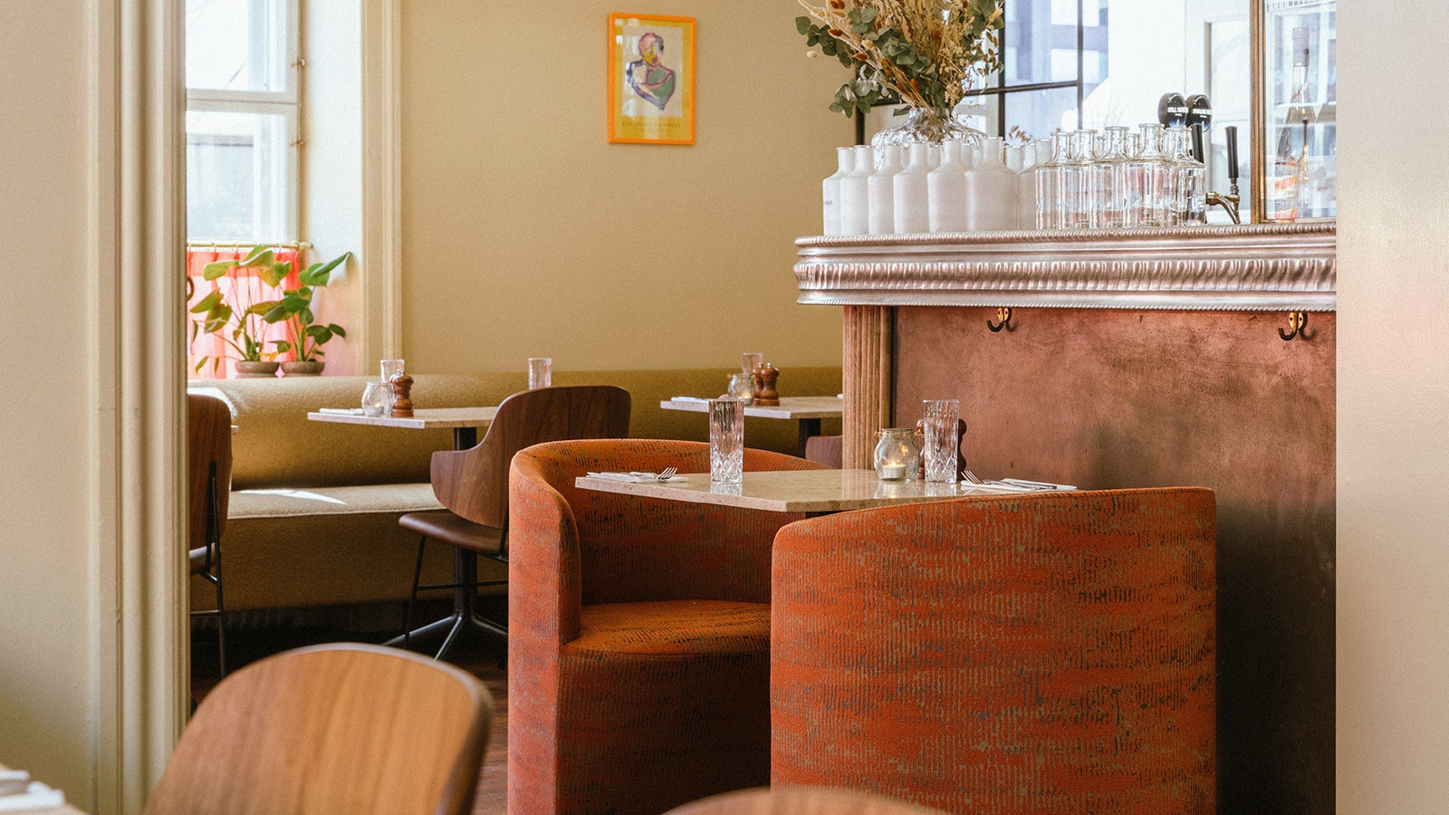 Cozy cafe interior with rust-orange curved upholstered chairs, marble tables, wooden chairs and glassware on a copper bar top