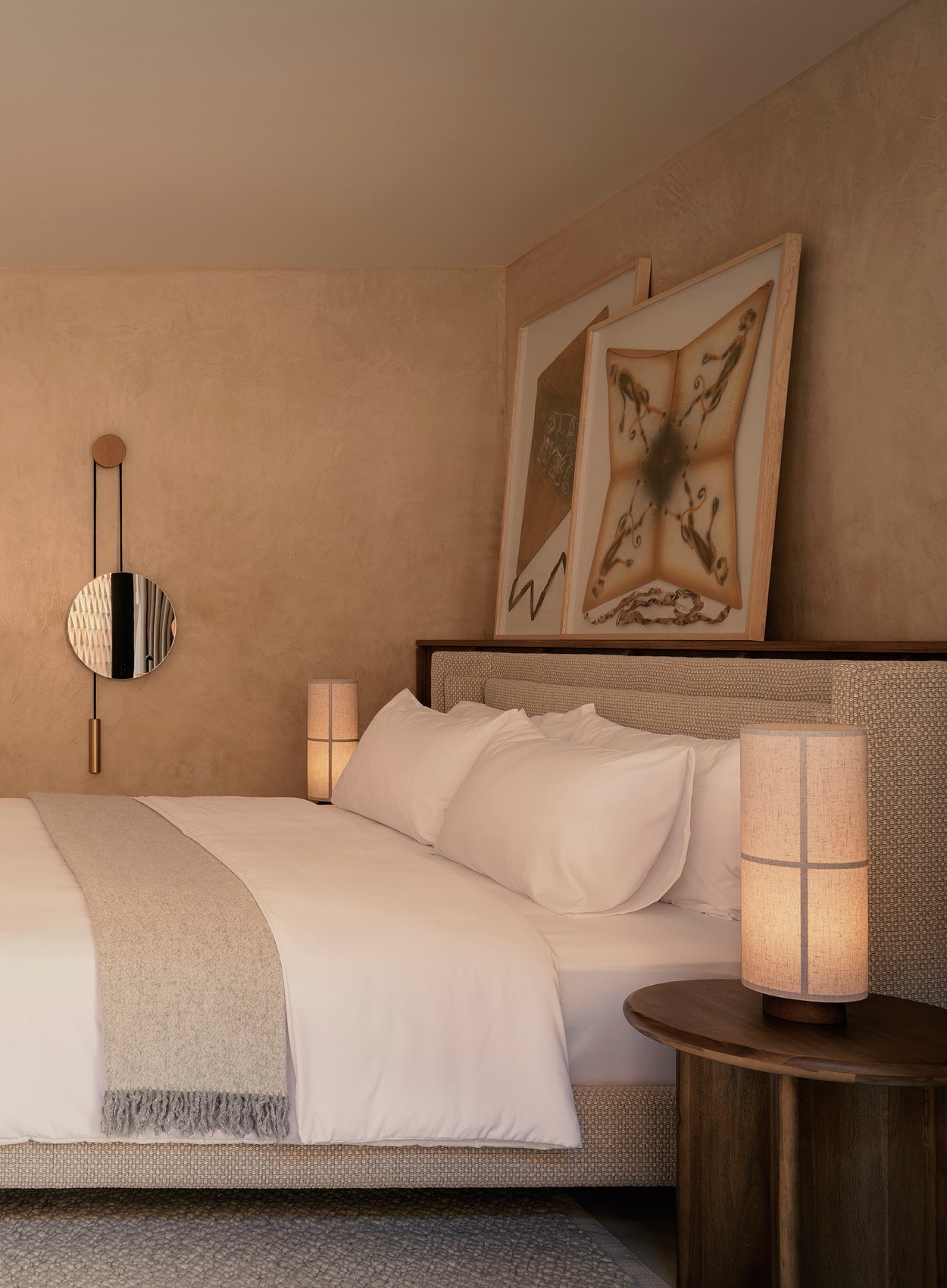 Neutral-toned bedroom with textured beige walls, upholstered bed, white linens, wool throw, bedside wooden lamp and leaning