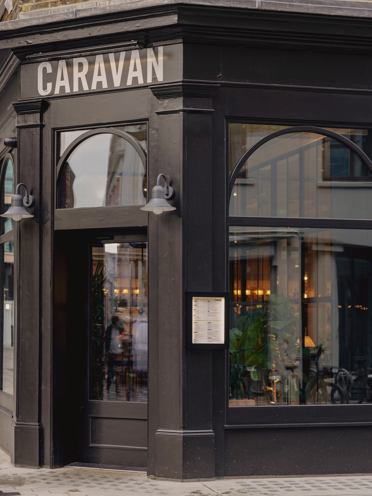 Black-painted corner storefront with arched windows, two grey wall lamps and white "CARAVAN" sign above entrance