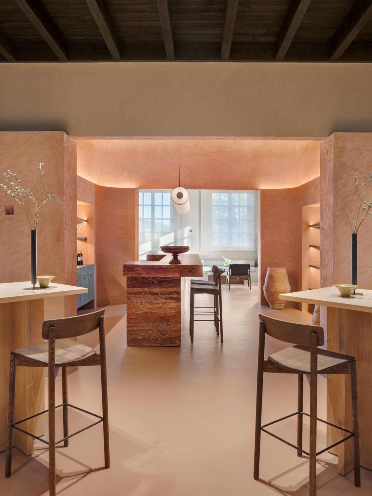 Minimalist warm-toned interior with terracotta plaster walls, wooden bar island, high stools and pendant light