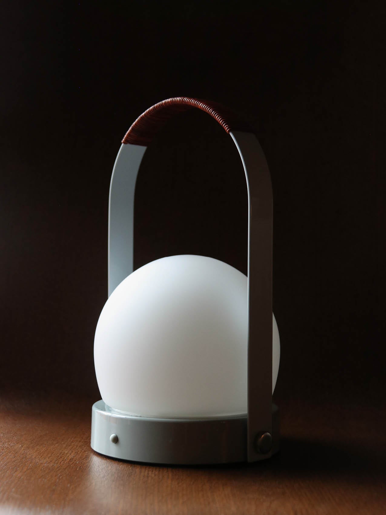 Carrie Portable Lamp featuring a white opal glass globe and leather handle, resting on a dark wooden surface.